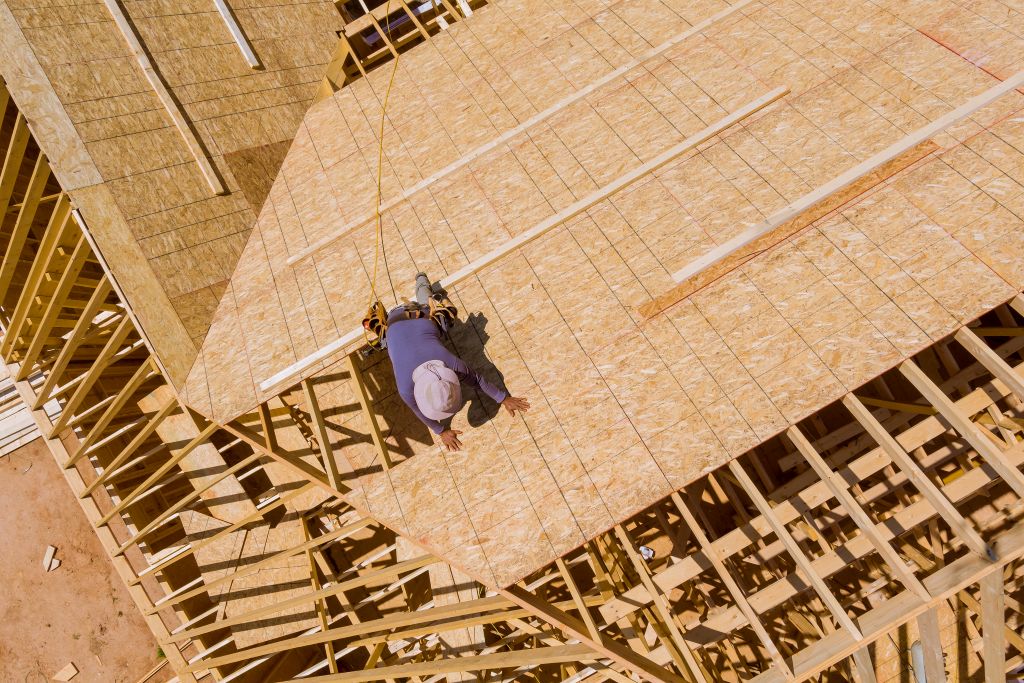 home-roof-construction-site-with-all-installed-new-2025-03-27-03-29-17-utc alt="man in hardhat on new roof in spring installing roof decking"