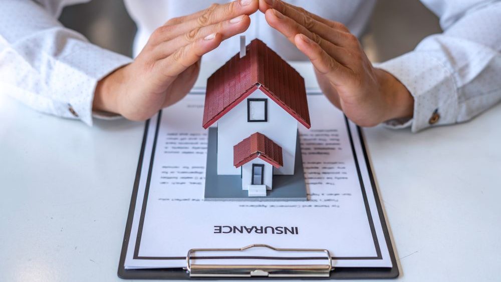 springtxroofers alt="hands over a mini house ontop of paperwork that says insurance"