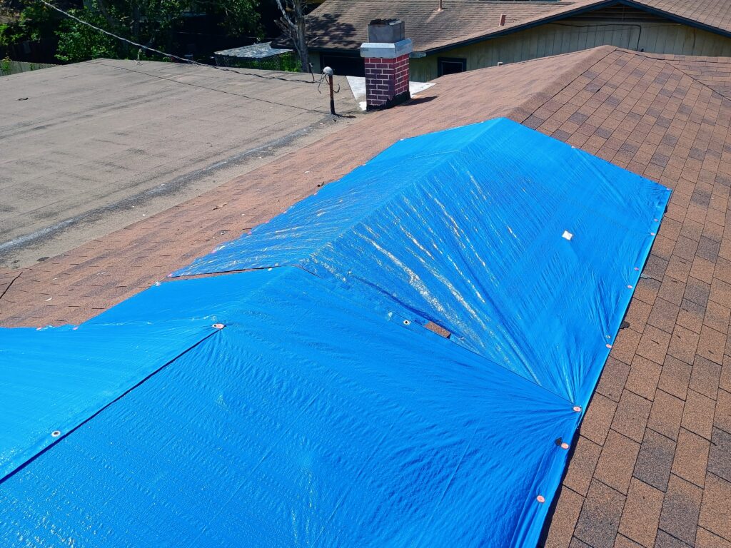 Large commercial-grade tarp covering a significant section of a residential roof in Tomball.